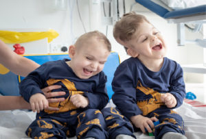 Yigit and Derman, two craniopagus twins, smile happily post-operation, they are in a hospital.