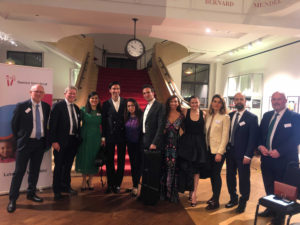 Attendees at the Gemini Untwined fundraiser, including Dr. Jeelani, pose for a group photograph. They are in the Wellcome Collection. A staircase with a red carpet lies in the background.